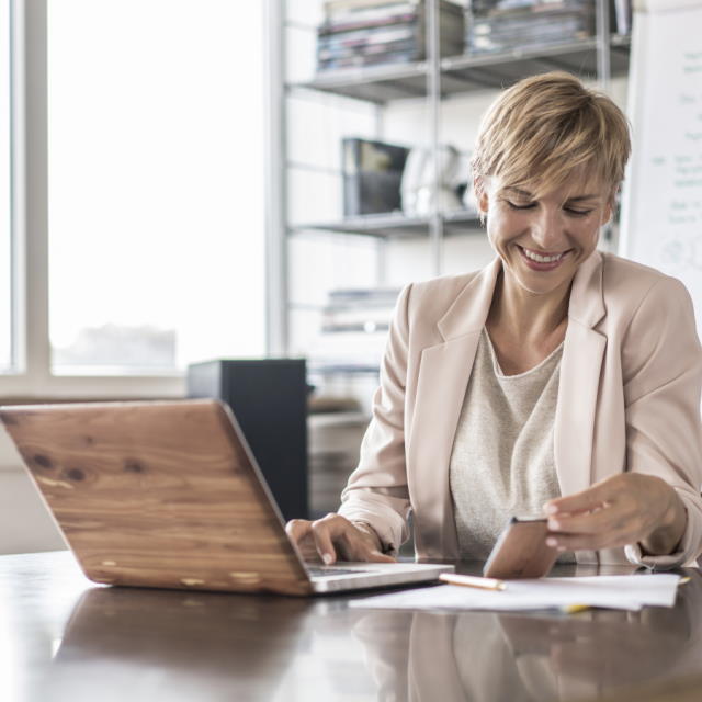 woman at desk on laptop and mobile